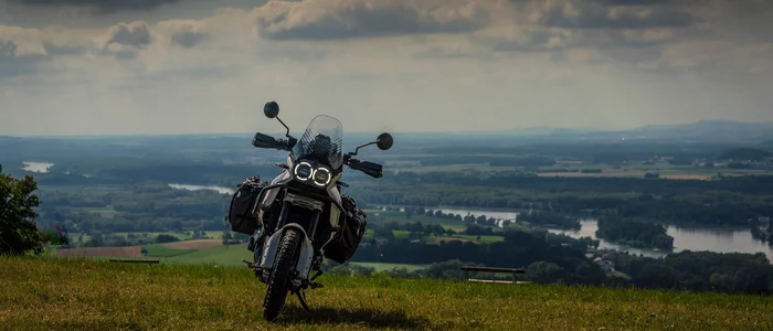 Wohlfühlhotel Rockenschaub **** © Moppetfoto.de Motorrad auf einer Wiese mit Blick auf eine Flusslandschaft unter wolkigem Himmel