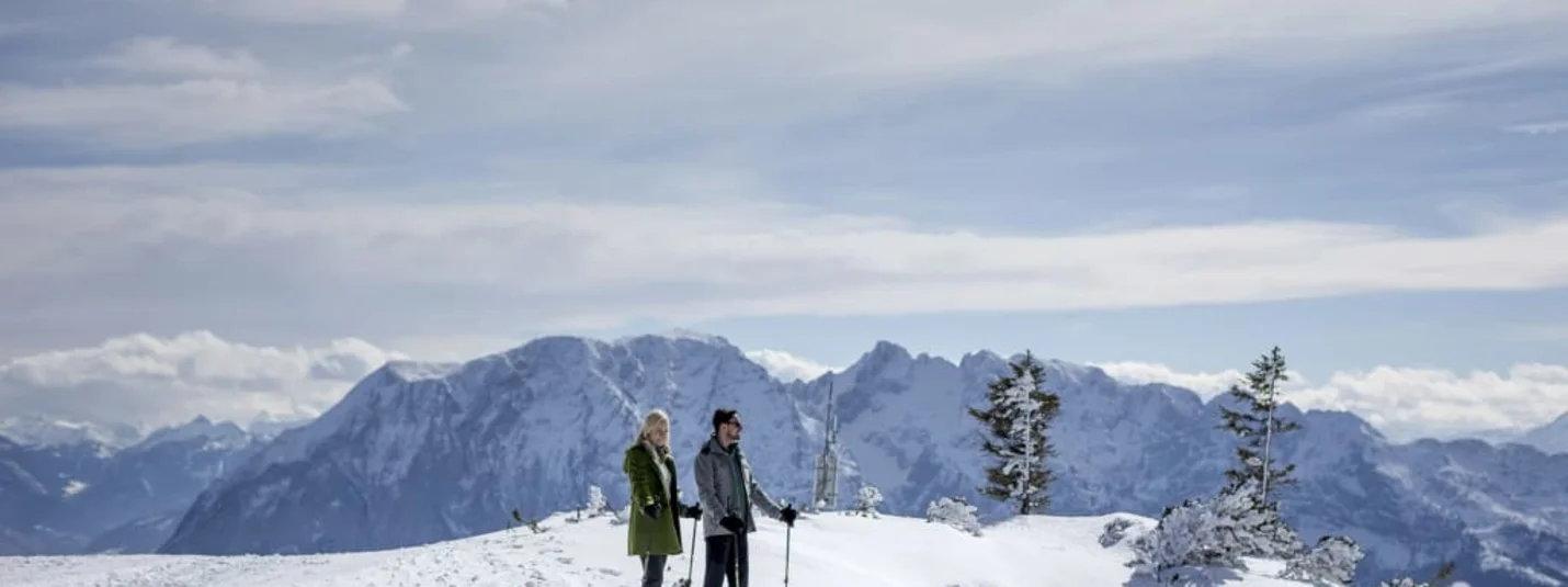 Zwei Wanderer mit Stöcken auf einem verschneiten Bergkamm vor Bergpanorama