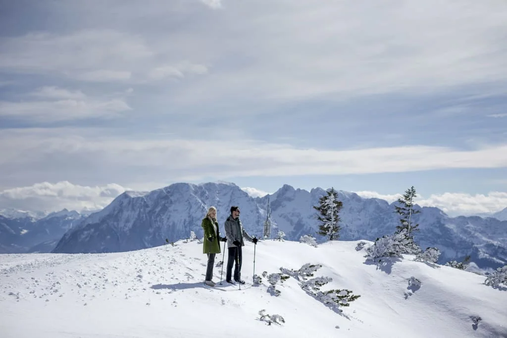 Winter magic on the mountain Two hikers with poles on a snowy mountain ridge against a mountain panorama