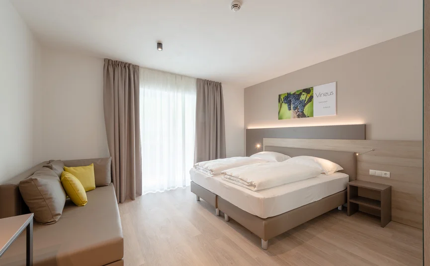 Modern bedroom with double bed, sofa, and light wood flooring