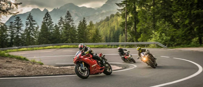 Drei Motorräder fahren auf kurviger Bergstraße bei bewölktem Himmel