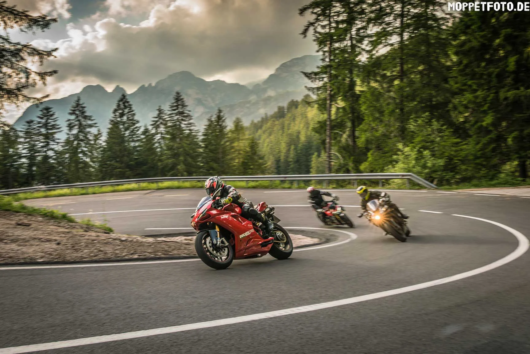 Hotels © Moppetfoto.de Three motorcycles riding on a winding mountain road with cloudy sky