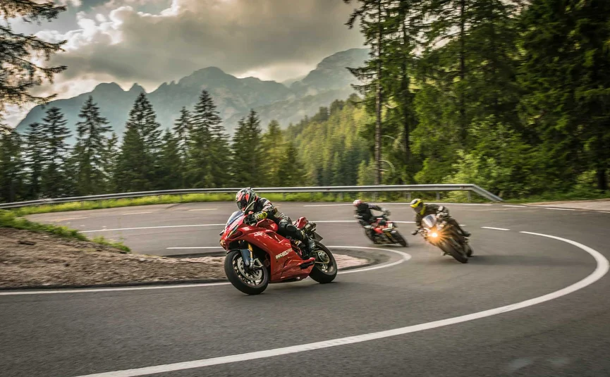 Three motorcycles riding on a winding mountain road with cloudy sky