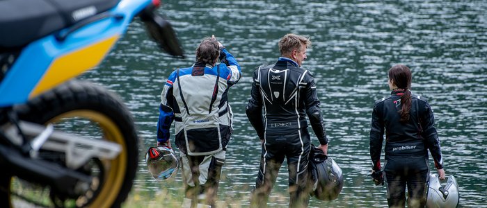 Drie motorrijders bij een meer met helmen, motoren deels zichtbaar