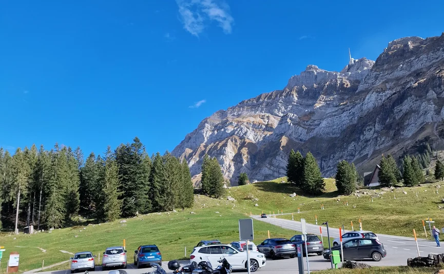 Parking lot with motorcycles and cars by forested mountain under clear blue sky