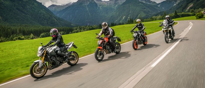 Motorradurlaub in Kärnten © Moppetfoto.de Vier Motorradfahrer fahren auf einer Bergstraße mit grünen Wiesen und bewölktem Himmel