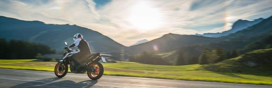 Motorradfahrer fährt auf Bergstraße bei Sonnenuntergang