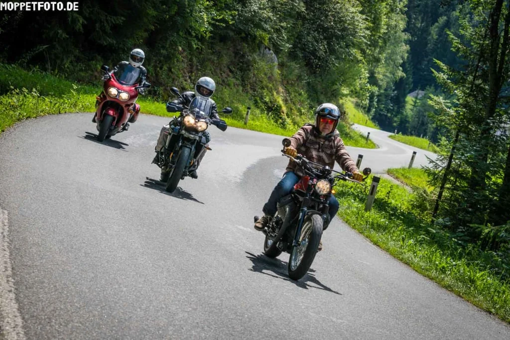 Three motorcyclists riding on a winding forest road