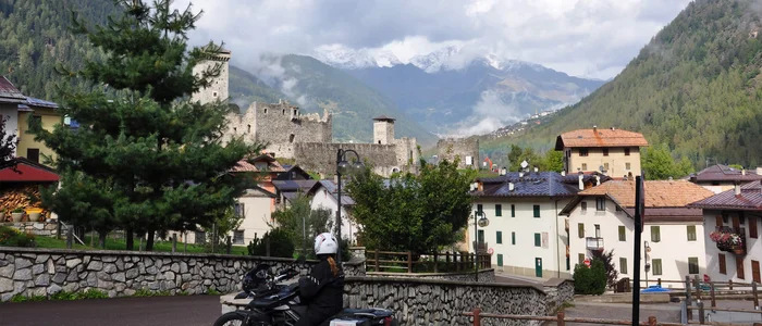 Motorradfahrer vor Schloss in einem Bergdorf mit Nebel und Wolken