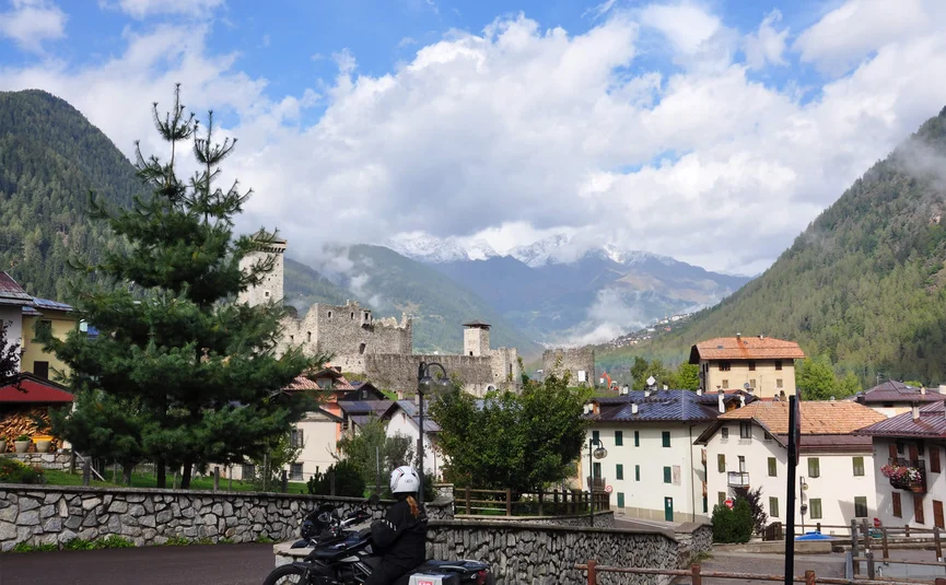 Motorcyclist near a castle in a mountain village with fog and clouds