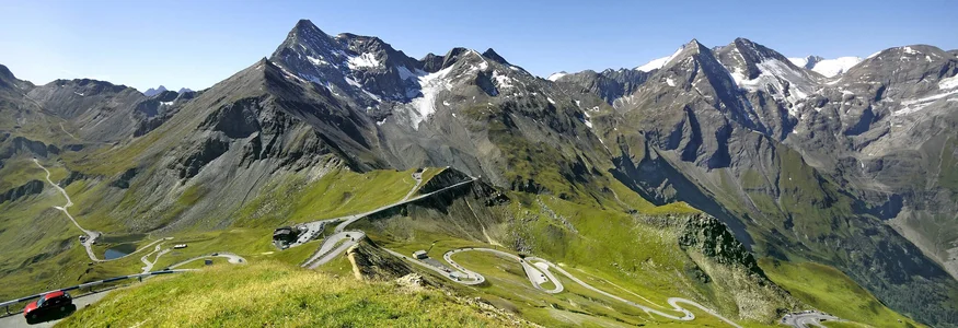 Serpentinenstraße in grünen Alpen mit schneebedeckten Bergen unter blauem Himmel