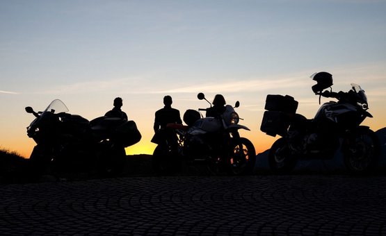 Three motorcycles and riders silhouetted at sunset on cobblestone road