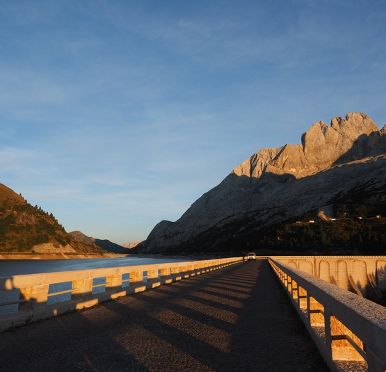 Staumauer mit Autostraße und Berglandschaft im Sonnenuntergang