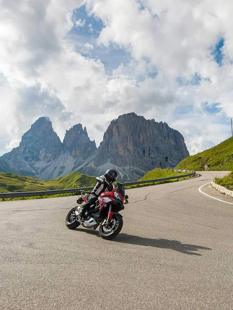 Motorcyclist riding mountain road with rocky peaks and cloudy sky