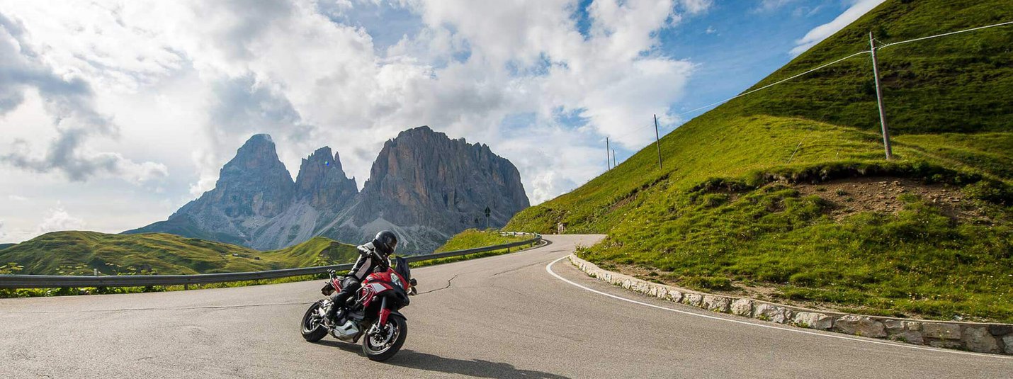 Motorrijder op bergweg met rotsachtige pieken en bewolkte lucht
