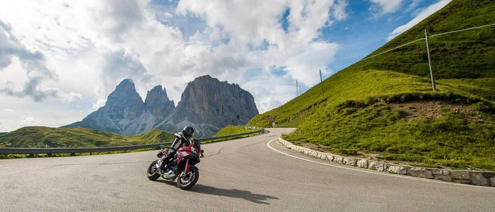 Motorcyclist riding mountain road with rocky peaks and cloudy sky