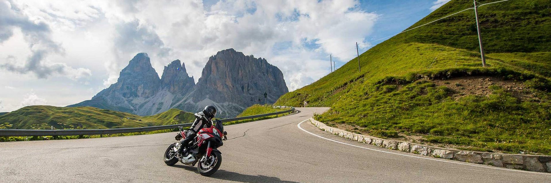 Hotel Florian ***S © Arik Oberrauch Motorradfahrer auf Bergstraße mit Felsen und bewölktem Himmel