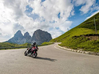 Sella Ronda - Alta Badia © Arik Oberrauch Motorcyclist riding mountain road with rocky peaks and cloudy sky