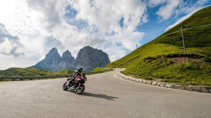Sella Ronda – Alta Badia © Arik Oberrauch Motorradfahrer auf Bergstraße mit Felsen und bewölktem Himmel