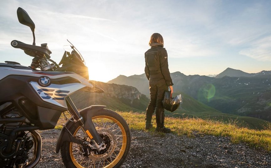 Motorcyclist holding helmet looking at mountain landscape at sunset