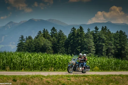 Twee motorrijders op een weg met bos en bergen op de achtergrond