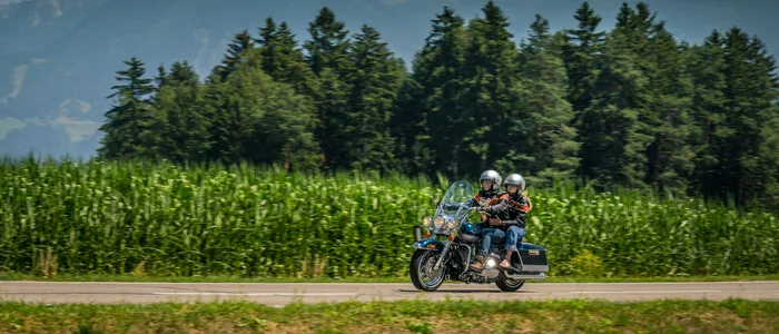 Two motorcyclists riding on a road with forest and mountains background