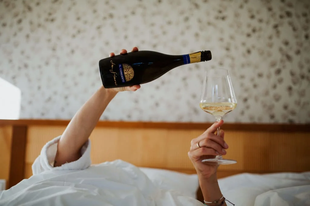 Du + Ich + Prosecco Person gießt Weißwein aus Flasche in Weinglas im Bett