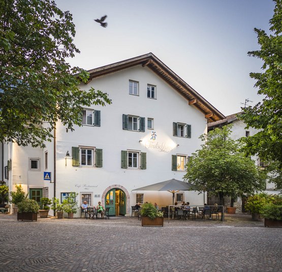 Adamello - Touren für Könner © Hannes Niederkofler Café mit Außensitzplätzen an einem kopfsteingepflasterten Platz umgeben von Bäumen