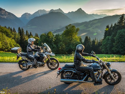 Twee motorrijders op bergweg met Alpen op achtergrond bij zonsondergang
