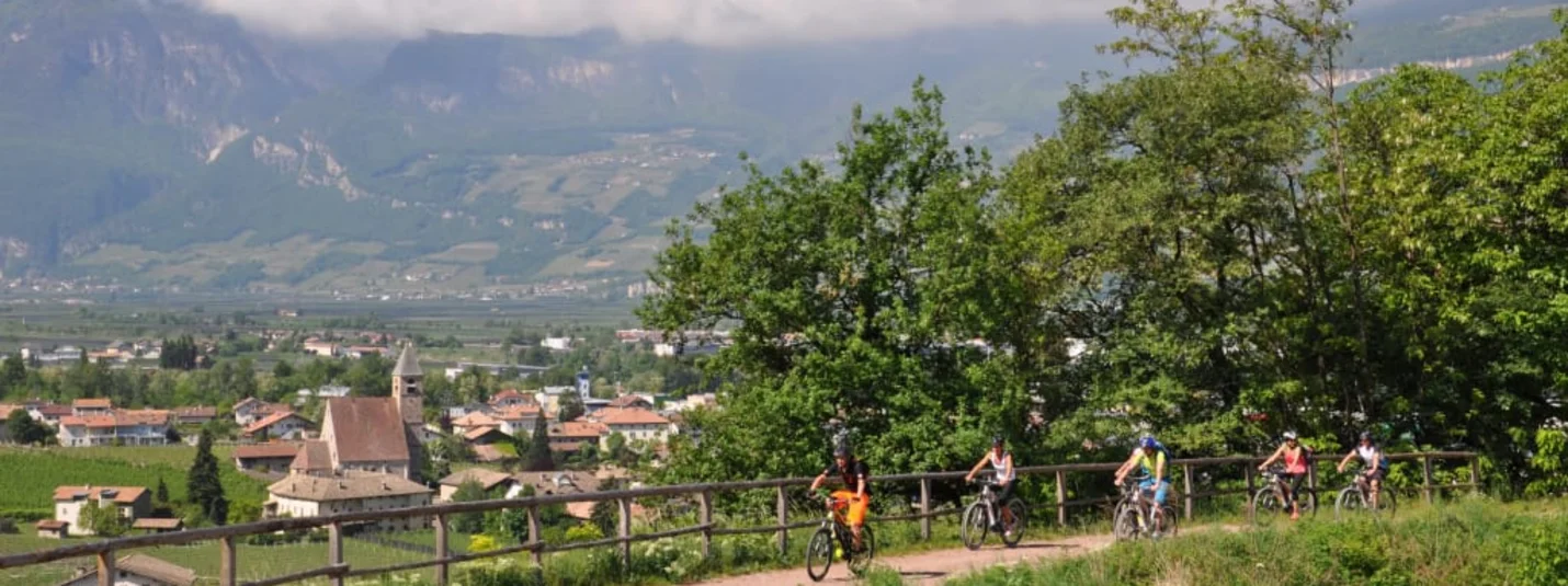 Holidays with e-bike Group cycling on path with mountain view and village below