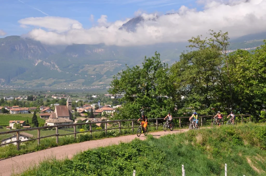Group cycling on path with mountain view and village below