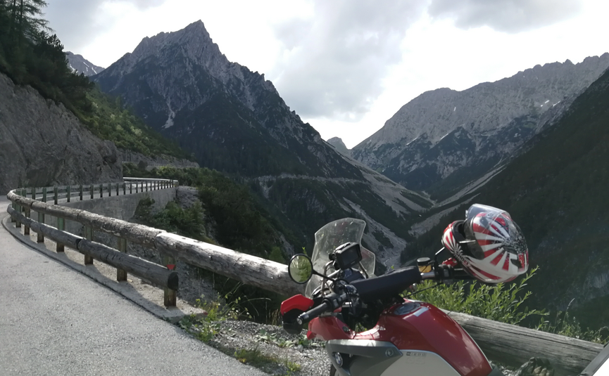Motorrad auf Bergstraße mit steilen Felsen und bewölktem Himmel