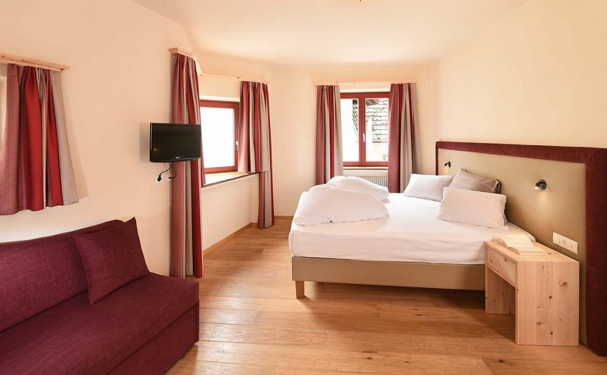 Helles Schlafzimmer mit Doppelbett, Fernseher und rotem Sofa