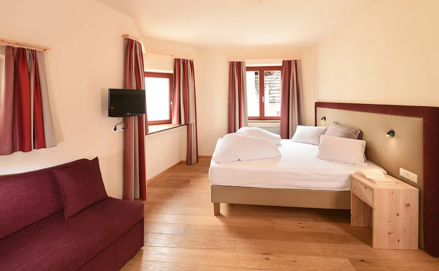 Bright bedroom with double bed, TV, and red sofa