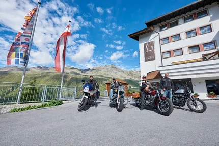 Vier Männer auf Motorrädern vor einem Hotel in den Alpen