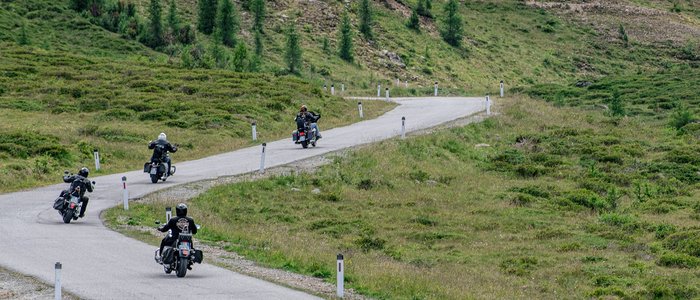 Vier motorrijders op een kronkelende weg door groen bergachtig landschap