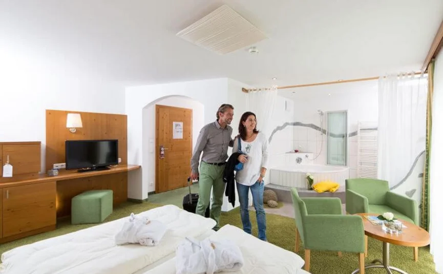Couple enters bright hotel room with double bed and seating area