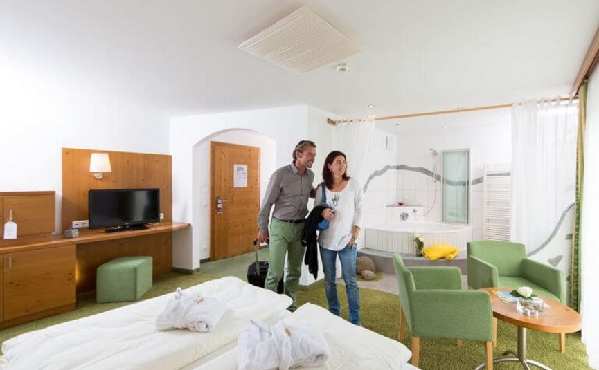 Paar betritt ein helles Hotelzimmer mit Doppelbett und Sitzecke