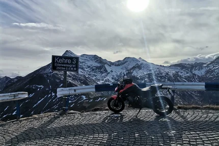 Motorcycle parked at Kehre 3 at 2503m with snow-covered mountains in background