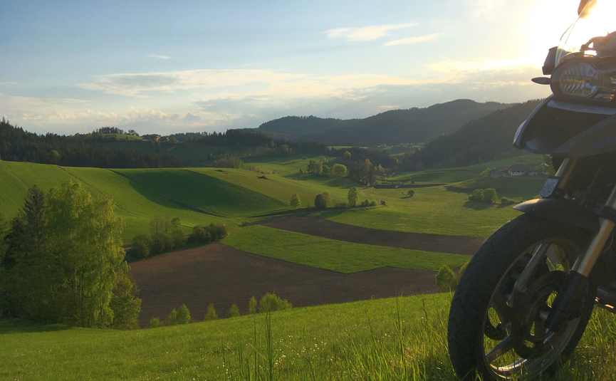 Motorcycle in foreground with green hills and valley at sunset