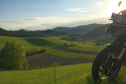 Motorfiets op de voorgrond met groene heuvels en vallei bij zonsondergang