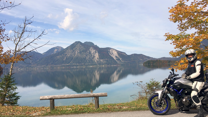 Motorradfahrer an See mit Bergspiegelung und Herbstbäumen