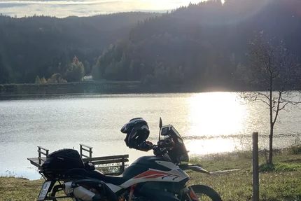 Motorcycle by lakeside at sunset with forested hills in the background