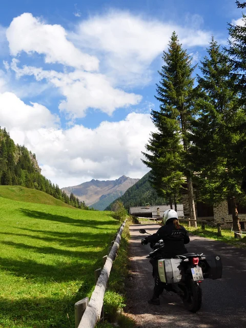 Motorcyclist on mountain road beside green valley and forested hills