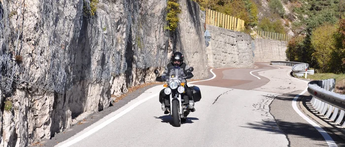 Motorcyclist riding on a winding mountain road beside rock wall