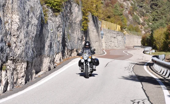 Motorradfahrer auf kurviger Bergstraße neben Felswand