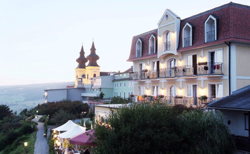 Hotelgebäude mit beleuchteten Balkonen und Kirche mit doppelten Türmen im Hintergrund