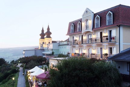 Hotel Rose © Hotel Rose Hotelgebäude mit beleuchteten Balkonen und Kirche mit doppelten Türmen im Hintergrund