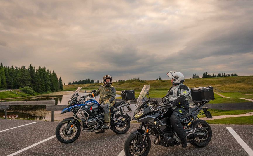 Zwei Motorradfahrer auf BMW-Motorrädern in einer Landschaft bei bewölktem Himmel
