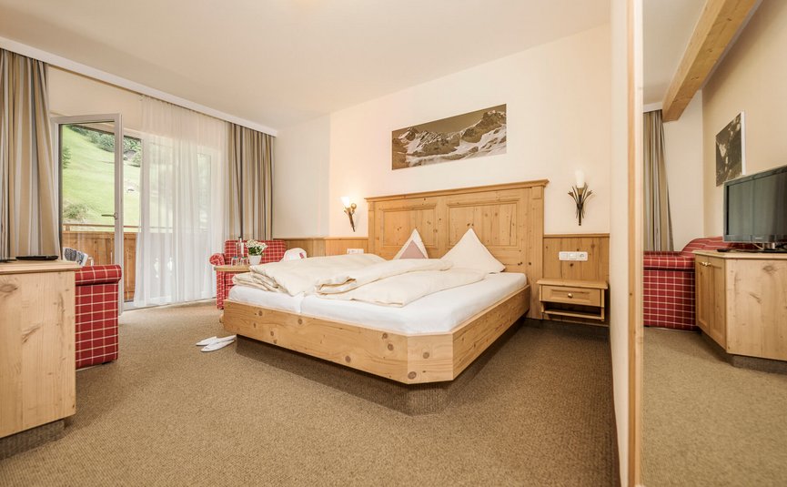 Gemütliches Hotelzimmer mit Holzmöbeln und Balkonblick auf grüne Wiese